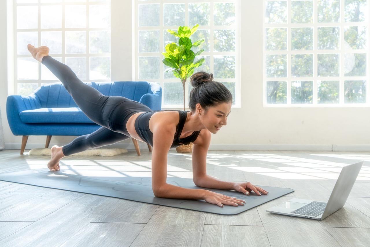 fit woman doing yoga plank and watching online tutorials on laptop, training in living room