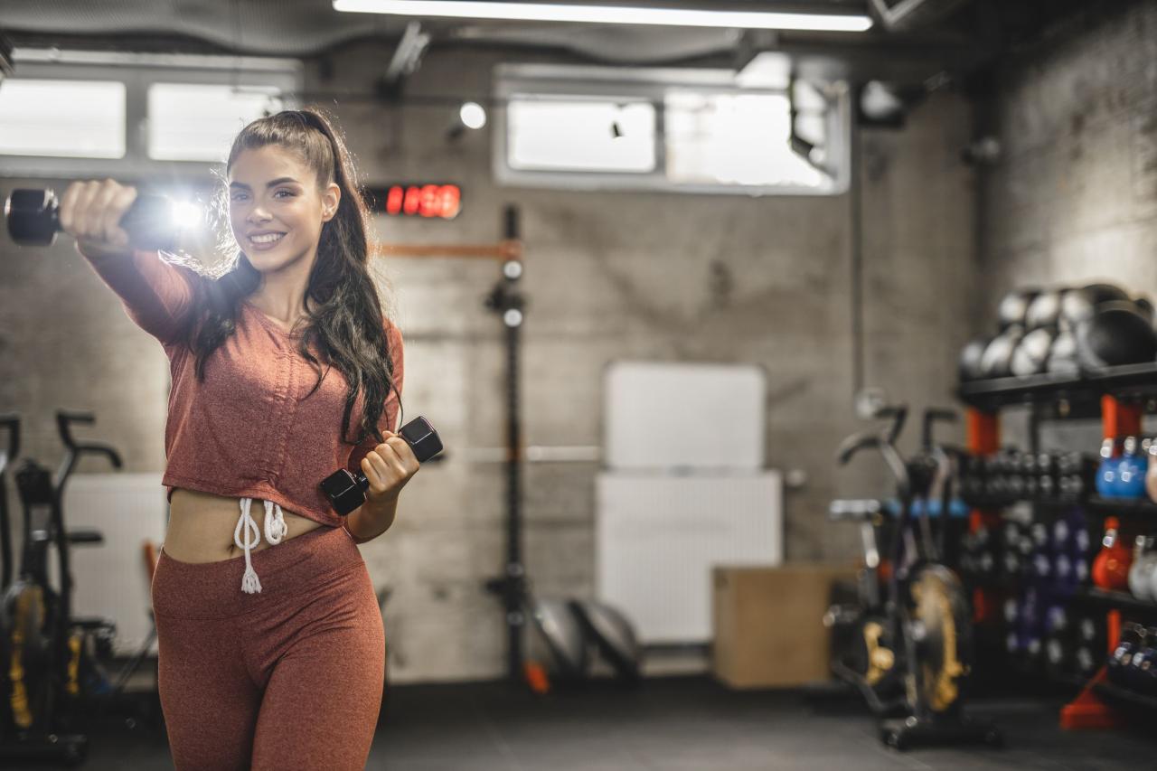 young sporty woman is having weight training with dumbbells at the gym