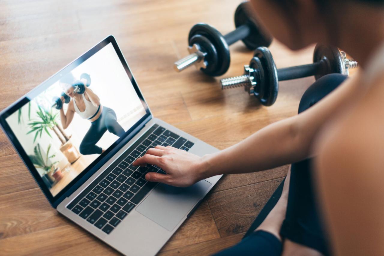 young woman practising weight training workout with a video lesson on laptop